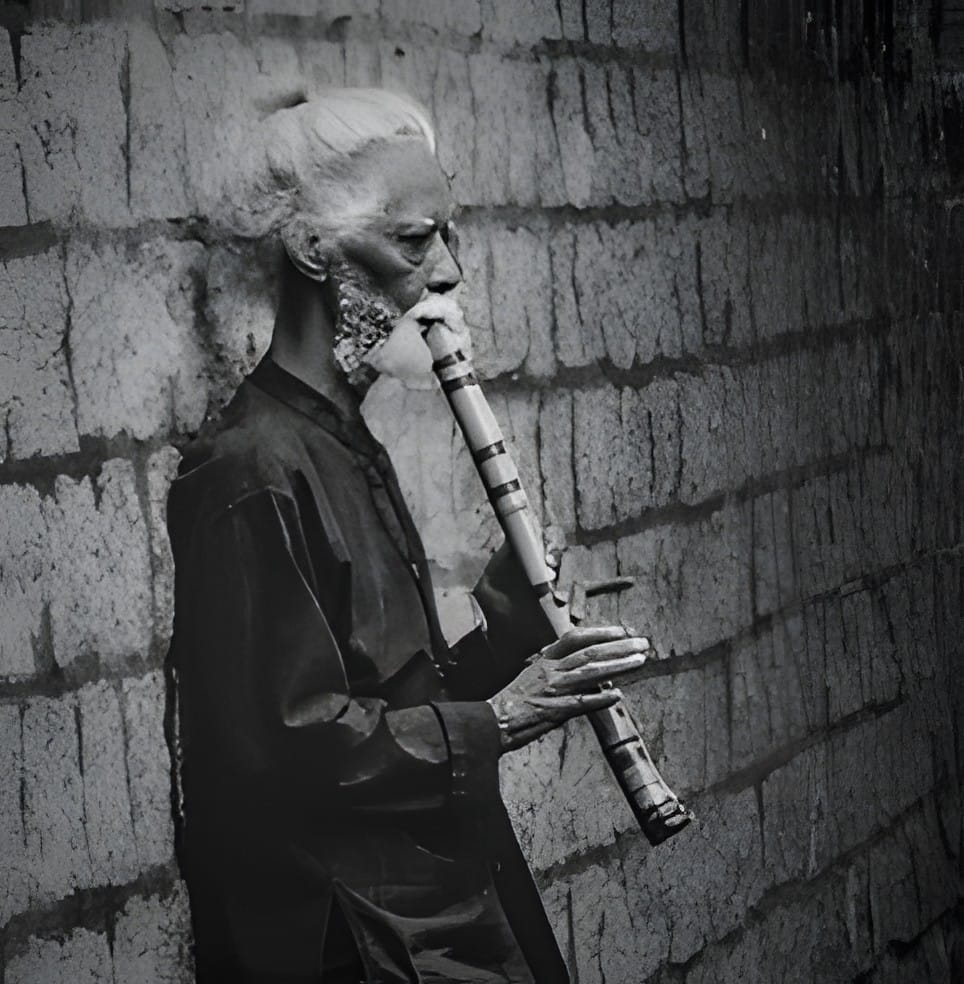 An older man playing a flute against a stone wall, black and white