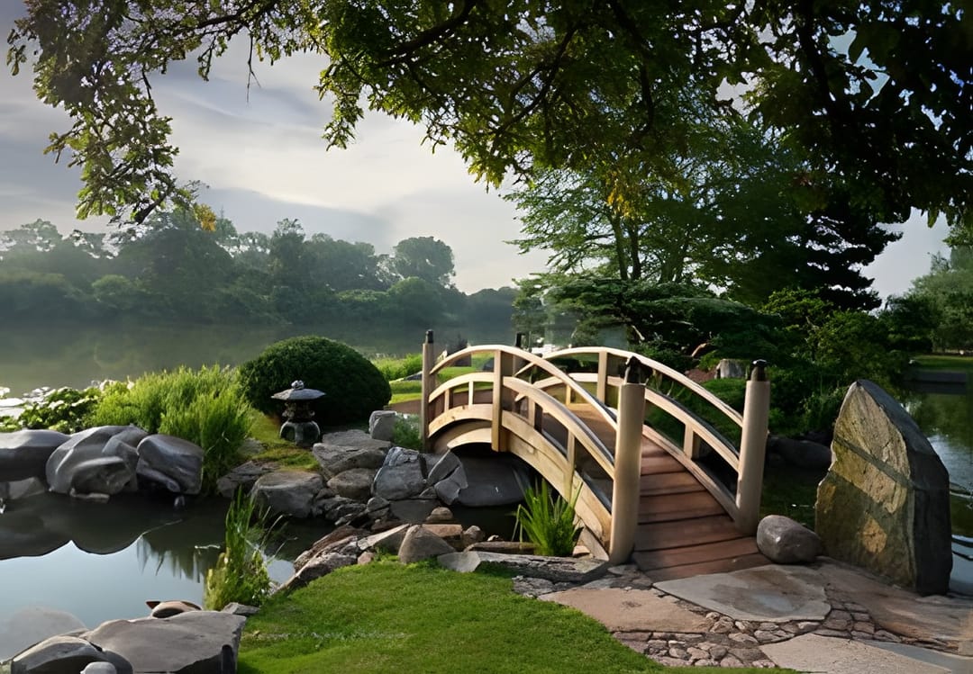 An arched wooden bridge over a still garden pond with autumn reflections