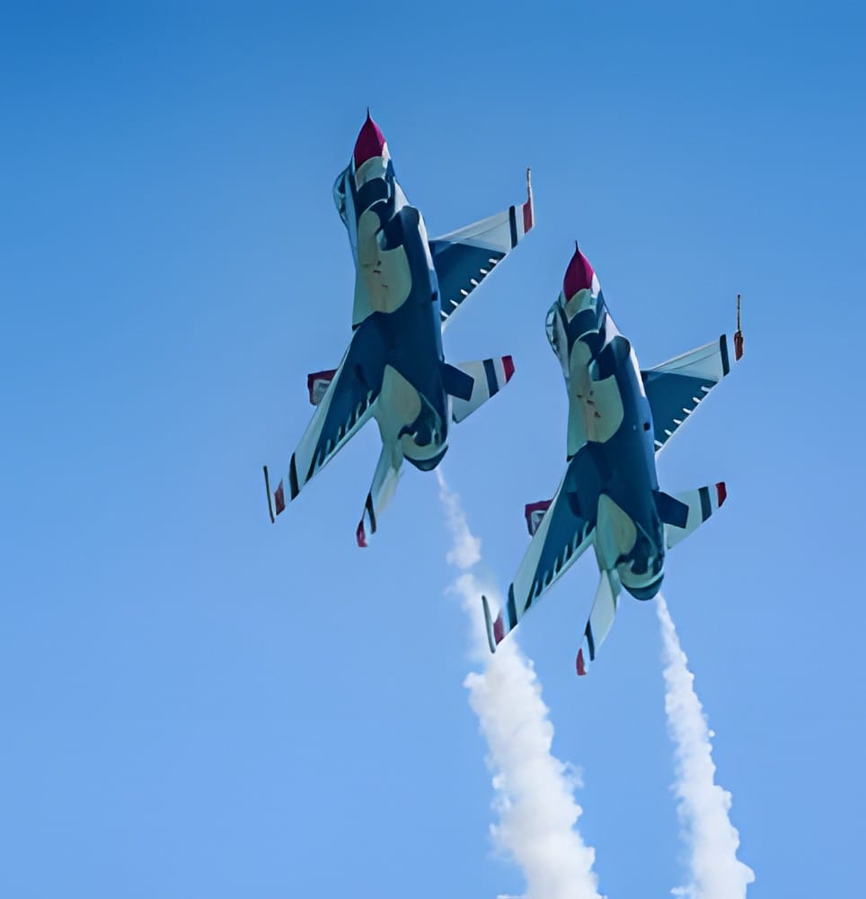 Two Air Force Thunderbirds jets climbing into a blue sky