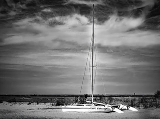 A sailboat beached under a dramatic sky, black and white
