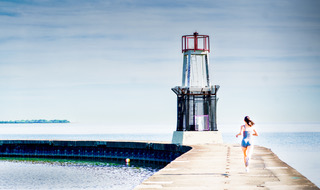 A runner approaching a small lighthouse beacon at the end of a pier, soft blue