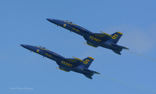 Two Blue Angels jets flying close together over the lake