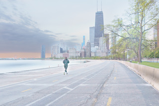 A lone runner on an empty lakefront road at dawn with the skyline beyond, soft pastel