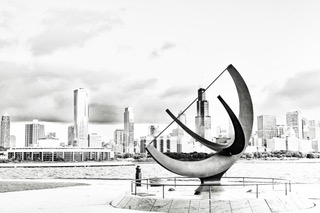 A sundial sculpture on the lakefront with the Chicago skyline behind, black and white