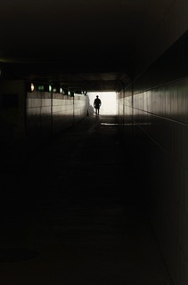 A lone figure silhouetted walking through a dark tunnel toward light